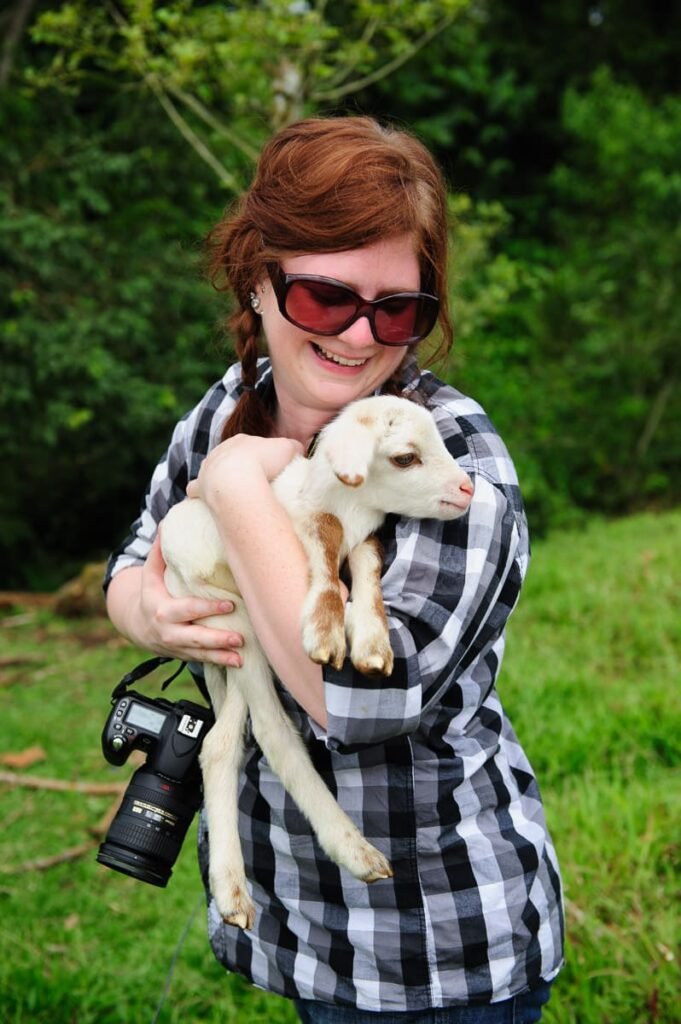 A smiling guest enjoying an authentic animal encounter, holding a friendly baby goat during the Tico Farm Morning Tour, one of the best things to do in La Fortuna with kids.